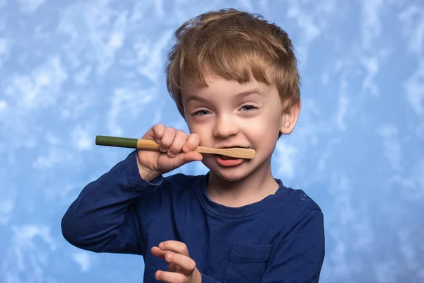 little child brushes teeth with a bamboo toothbrush in the bathroom on a blue texture background. horizontal photo. ecologicaly clean. morning hygiene concept.