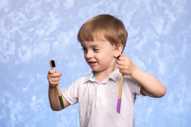 Küçük bir çocuk banyoda iki bambu diş fırçasını tutuyor ve inceliyor. Ekolojik olarak temiz. Sabah hijyen konsepti.