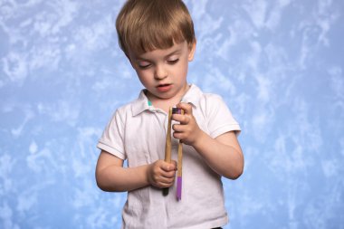 Küçük bir çocuk banyoda iki bambu diş fırçasını tutuyor ve inceliyor. Ekolojik olarak temiz. Sabah hijyen konsepti.