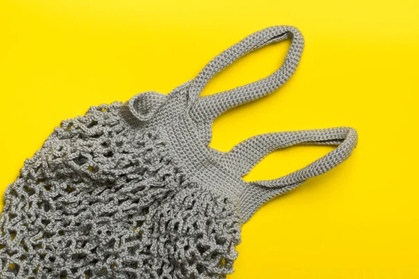 gray knitted bag string bag lies on a yellow background. flatley. eco friendly concept zero waste