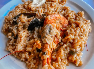 Restorandaki masada karides ve midyeyle pişirilmiş bir İspanyol yemeği var. Restoran menüsü veya İspanyol yemekleri üzerine makaleler.