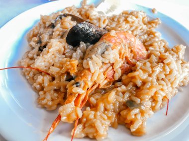 Restorandaki masada karides ve midyeyle pişirilmiş bir İspanyol yemeği var. Restoran menüsü veya İspanyol yemekleri üzerine makaleler.
