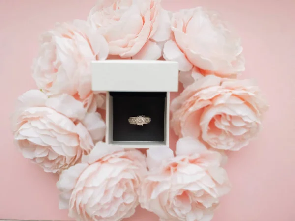 In the jewelry box there is a ring in a frame of pink delicate peonies on a beautiful pink background. Romantic concept. Flat style.