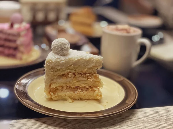 Piece of white cake with sponge cake, coconut flakes and decoration on top of the cake in the form of a ball on a plate in a restaurant.