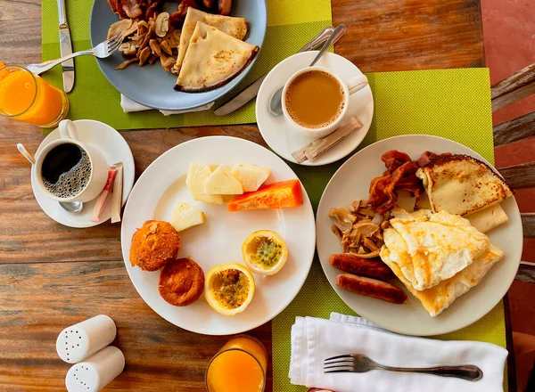 Breakfast in the hotel restaurant on the table with scrambled eggs, bacon, pancakes, sausages, mushrooms, coffee, juice and fruit pineapple, papaya, passion fruit