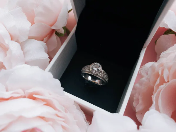 In the jewelry box there is a ring in a frame of pink delicate peonies on a beautiful pink background. Romantic concept.