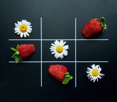 Papatya çiçekleri ve çileklerden yapılmış siyah bir arka planda tik tak parmak. Düz yatıyordu. Doğal konsept.