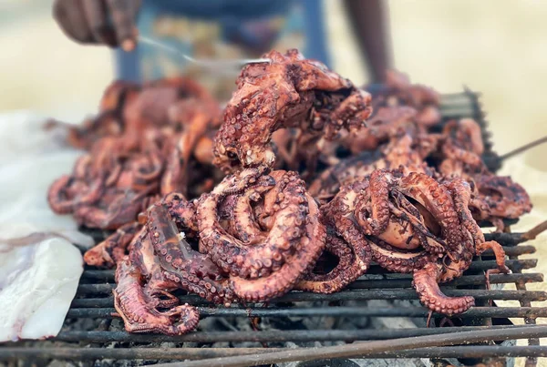 Primer plano de los pulpos en las manos de un hombre frito en una parrilla en la orilla del océano — Foto de Stock