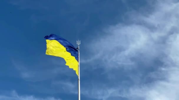 Kiev, Ucrânia, a bandeira do estado da Ucrânia, azul e amarelo, bem como o brasão de armas do país contra o fundo de um céu azul brilhante balançando no vento — Vídeo de Stock