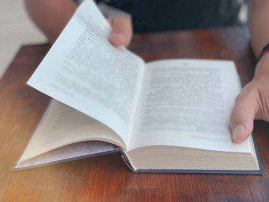 Ahşap bir masada oturup kitap okuyan bir adamın yakın çekimi.