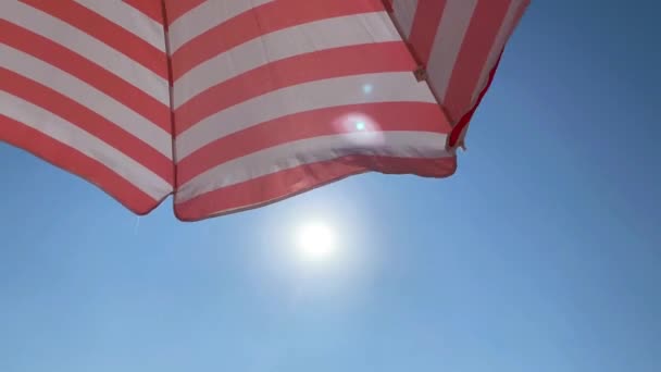 Parte de un paraguas de playa a rayas contra un hermoso cielo azul y sol. Concepto de turismo y verano — Vídeo de stock