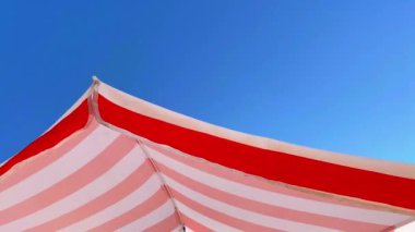 Güzel mavi gökyüzüne ve güneşe karşı çizgili bir sahil şemsiyesi. Turizm ve yaz konsepti