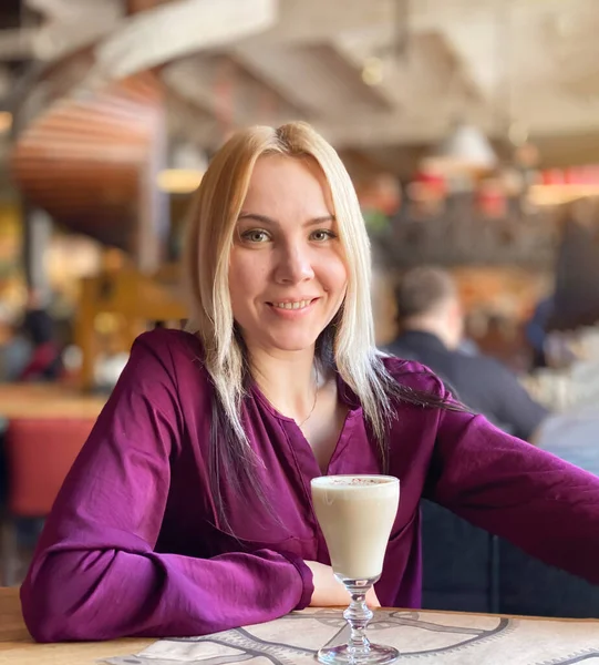 Una chica rubia en un suéter lila se sienta en un acogedor restaurante — Foto de Stock
