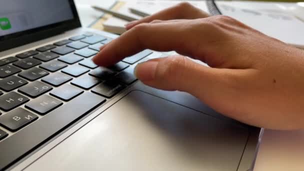 Közelkép egy nőről, aki egy laptopnál dolgozik, és gépel valamit a billentyűzeten, miközben jegyzetel egy jegyzetfüzetben. — Stock videók
