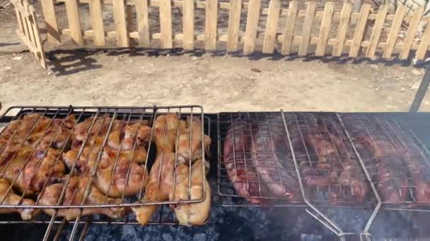 On the grill on the territory of a private house in the courtyard, chicken and pork sausages are cooked and pleasant smoke from the barbecue is visible — Stock Video