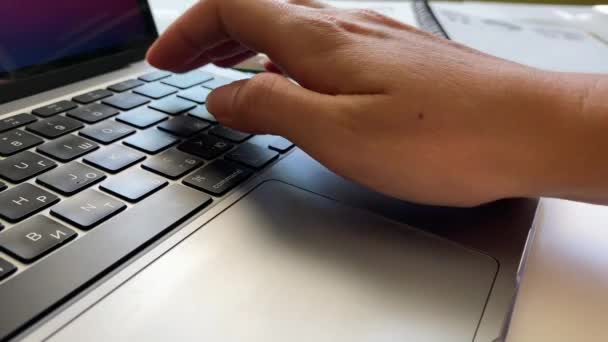 Primer plano de una mujer que trabaja en un ordenador portátil y escribe algo en el teclado mientras toma notas en un cuaderno — Vídeos de Stock
