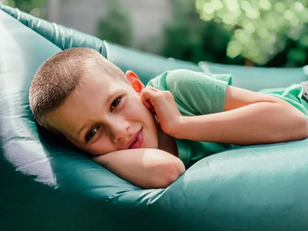 Ritratto di un ragazzo caucasico di 7 anni con una t-shirt verde appoggiata su un lettino gonfiabile lamzak. — Foto Stock