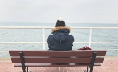 Kışın ceketli, şapkalı ve sırt çantalı genç bir adam iskelede duruyor ve Baltık Denizi 'ne bakıyor.