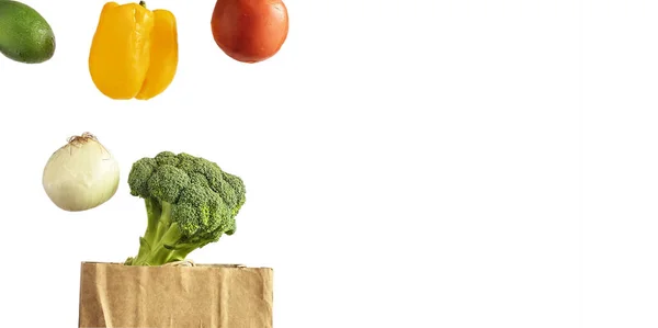 Aislado sobre fondo blanco levitando verduras tomate, pimienta, aguacate, cebolla, brócoli sobre una bolsa de papel — Foto de Stock