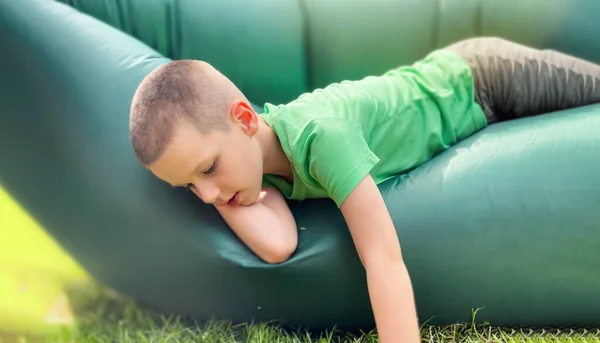 Retrato de um menino caucasiano 7 anos de idade em uma camiseta verde descansando em um lamzak, espreguiçadeira inflável. — Fotografia de Stock