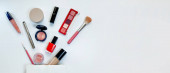 Krásný koncept. Make-up produkty stíny, zvýrazňovač, červeň, štětce, prášek, lesk, řasenka, lesk, rtěnka, tužka a bílá dárková taška na bílém pozadí