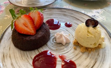 Lezzetli ve güzel kaplanmış bir gurme tatlı içinde zengin bir çikolatalı lav keki ya da taze dilimlenmiş çilek ile süslenmiş bir şekerleme. Yanda, bir kepçe kremalı vanilyalı dondurma...