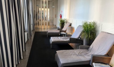 Modern spa rahatlama salonu iç mekanı. Üç rahat hasır şezlonglar yumuşak yastıklar, saksı bitkileri ve şık siyah beyaz çizgili perdeler sağIık için sakin bir atmosfer yaratır.