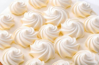 Beyaz arka planda çırpılmış krem buklelerle süslenmiş güzel pastanın tepesi.