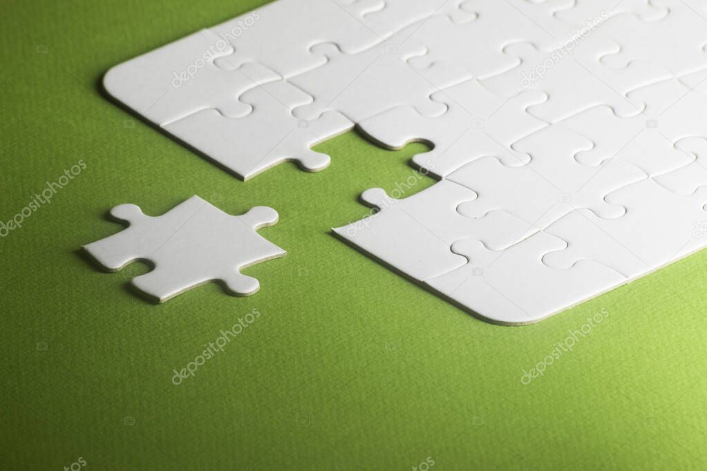 A white puzzle with one piece missing but not fitting. green background, copy space