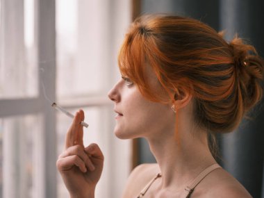 Penceresinde sigara olan genç ve güzel bir kadın. 
