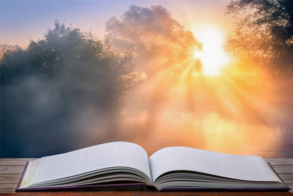 Open book against nature landscape with sunrise