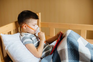 Bir çocuk akciğer solunumu sırasında tabletle oynuyor. İlaç ve bakım
