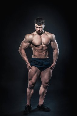 Stüdyoda siyah arka planda poz veren seksi genç bir atlet. Fitness, vücut geliştirme