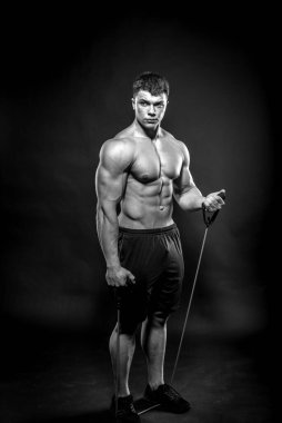 Stüdyoda siyah arka planda poz veren seksi genç bir atlet. Fitness, vücut geliştirme, siyah beyaz