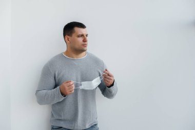 Genç bir adam, karantina sırasında maske takarak gri arka planda duruyor. Maskeli karantina