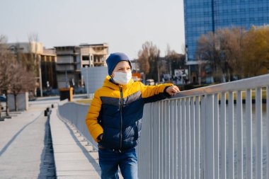 Bir çocuk, karantina sırasında maske takmış gri bir arka planda duruyor. Maskeli karantina