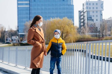 Genç bir aile, karantina ve salgın sırasında güneşli bir günde yürüyüp temiz hava soluyor. İnsanların yüzlerindeki maskeler.