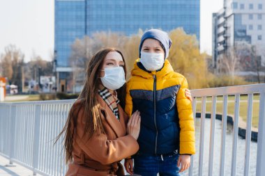 Genç bir aile, karantina ve salgın sırasında güneşli bir günde yürüyüp temiz hava soluyor. İnsanların yüzlerindeki maskeler.