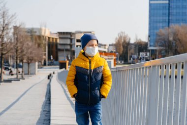 Bir çocuk, karantina sırasında maske takmış gri bir arka planda duruyor. Maskeli karantina