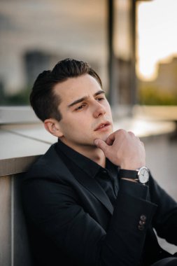 Şık bir genç adam gün batımında aynalı bir binanın yanında duruyor. Moda.