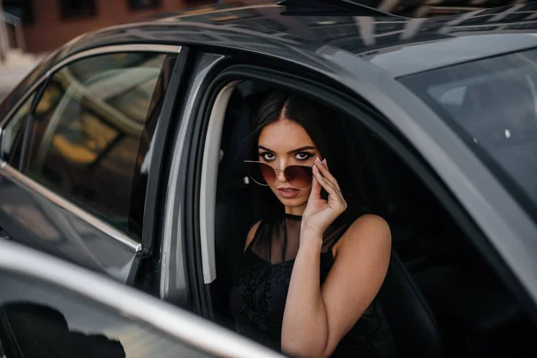 黒のドレスでビジネスクラスの車の中に座ってスタイリッシュな若い女の子 ファッション スタイル — ストック写真