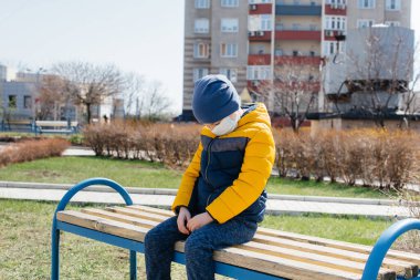 Karantina sırasında maskeli küçük bir çocuk oyun alanında yürüyor. Evde kal.