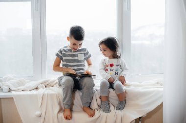 Erkek ve kız kardeş pencere kenarında oturuyorlar ve kitap okuyorlar. Mutluluk, aile