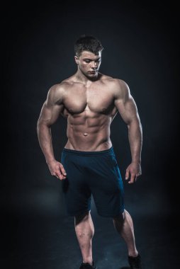 Stüdyoda siyah arka planda poz veren seksi genç bir atlet. Fitness, vücut geliştirme