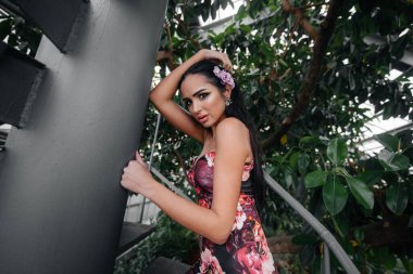 Genç ve güzel bir esmer botanik bahçesindeki sarmal bir merdivenin yanında tropik ormanın sık çalılıklarının arasında poz veriyor. Spa