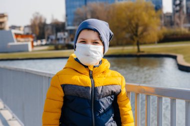 Bir çocuk, karantina sırasında maske takmış gri bir arka planda duruyor. Maskeli karantina