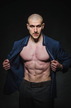 Tarz sahibi, kel genç bir adam çıplak bir gövdeyle kategoride karanlık bir arkaplanda duruyor.