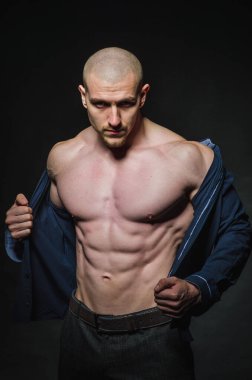 Tarz sahibi, kel genç bir adam çıplak bir gövdeyle kategoride karanlık bir arkaplanda duruyor.