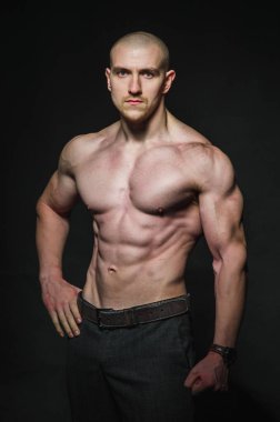 Sportif seksi adam karanlık bir zeminde üstsüz duruyor. Spor, güzellik