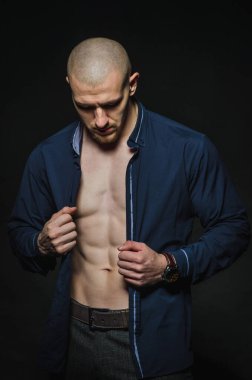 Tarz sahibi, kel genç bir adam çıplak bir gövdeyle kategoride karanlık bir arkaplanda duruyor.